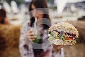 Vegan burger in hands closeup. Stylish hipster girl holding delicious vegan burger and smoothie in glass jar in hands at street