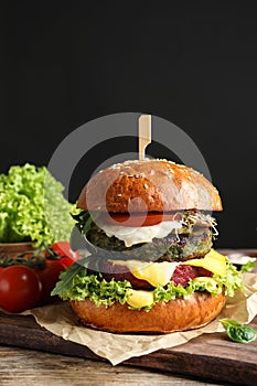 Vegan burger and vegetables on table against dark background.