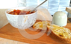 Vegan chili in a bowl sitting on a cutting board with toast on the side