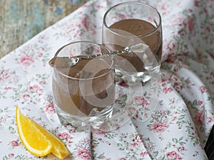 Vegan chocolate mousse desserts with orange in a glass with a spoon, fresh slises of orange on a light background