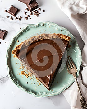 vegan chocolate pie on a light green plate, placed on a marble table, around it there are pieces of chocolate.