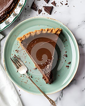 vegan chocolate pie on a light green plate, placed on a marble table, around it there are pieces of chocolate.