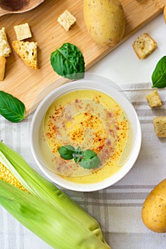 Vegan corn potato cream soup garnished with paprika, chili flakes and basil leaves.