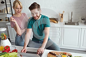 vegan couple with laptop buying goods online together in kitchen