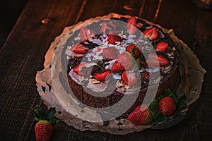 Vegan and delicious chocolate cake with strawberries, cocnut shovel and raspberry seeds, served on a paper serviette