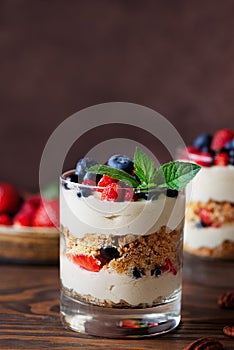 Vegan dessert in a glass with berries, mint, whipped cream and biscuit on a brown background. Healthy food, sugar, gluten and