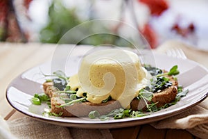 Vegan eggs benedict dish with plant-based sauce, whole grain bread, smoked tofu, young onion, greens, pea sprouts