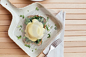 Vegan eggs benedict dish with plant-based sauce, whole grain bread, smoked tofu, young onion, greens, pea sprouts