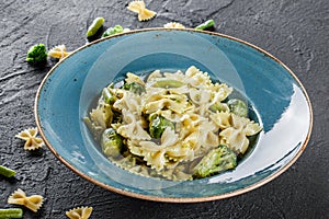 Vegan Farfalle pasta in a spinach sauce with broccoli, brussels sprouts, green beans in plate on dark stone background. Top view