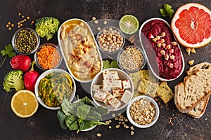 Vegan food background. Vegetarian snacks: hummus, beetroot hummus, green peas dip, vegetables, cereals, tofu. Top view, dark back