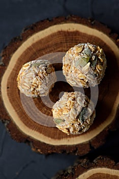 Vegan food concept. Close up of frozen oatmeal energy balls with pumpkin seeds on oak wood slab on black background top view