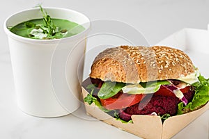 Vegan food delivery. Vegan beetroot burger with avocado in eco paper box with pea cream soup in disposable cup