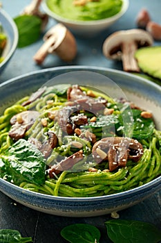 Vegan garlic mushroom pasta with spinach and avocado pesto drizzled with sesame seeds and roasted pine nuts