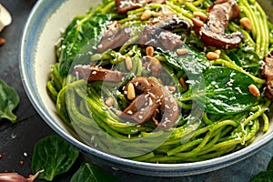 Vegan garlic mushroom pasta with spinach and avocado pesto drizzled with sesame seeds and roasted pine nuts