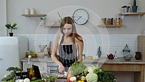 Vegan girl cooking salad with raw vegetables while looking on digital tablet for online recipe