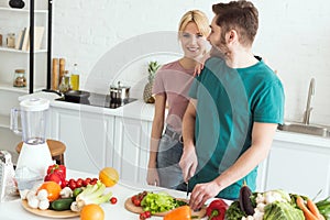 vegan girlfriend hugging boyfriend while he cutting vegetables