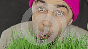 Vegan guy in a bright hat eats green grass