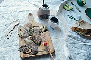 Vegan linnen crackers on a wooden board together with calabash, saucer, plate, cutlery lieing on a rough linnen fabric