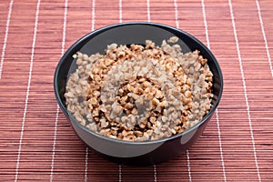 Vegan low calorie food, baked buckwheat in black round bowl studio shot on brown straw mat