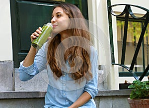 Vegan meal and detox break time concept. Beautiful girl sitting outside her home drinking green juice. Healthy detox vegan diet