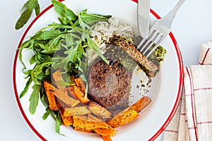 Vegan meatless cutlet with pesto, baked sweet potato wedges, rice and salad