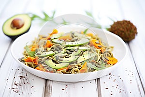 vegan pasta salad with avocado slices and pumpkin seeds, on a white table