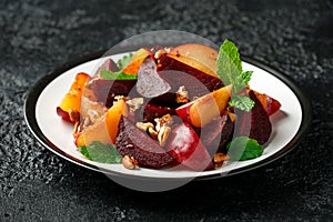 Vegan Plum, beet salad with pecan nuts, mint and herbs on rustic black table