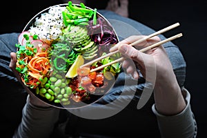 Vegan poke bowl with marinated watermelon, edamame, avocado, seaweed and carrot noodles. Man holding plate and chopstick