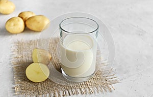 Vegan potato milk in a glass and potatoes on burlap on the wooden background, non-dairy alternative milk