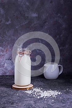 Vegan rice milk in a glass bottle and rice in a white plate on a wooden stand with a molon