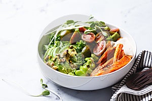 Vegan salad bowl with baked sweet potato, edamame beans, tomatoes, avocado, nuts, tahini dressing and sprouts