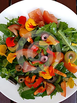 Vegan salad with wild herbs, edible blossoms, olives and tomatoes