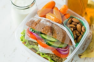 Vegan sandwich in lunch box with carrots and nuts