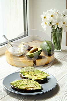 Vegan sandwich, rye bread toast, avocado, whole & halved, vegenaise sauce. Toasted sourdough, eggless mayonnaise, wood slice, daff