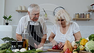 Vegan senior couple cooking salad with raw vegetables. Looking on digital tablet for online recipe