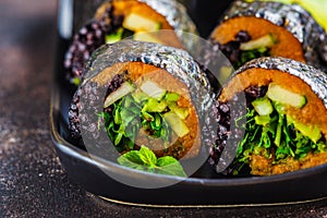 Vegan sushi rolls with black rice, avocado and sweet potato on black dish. Vegan food concept