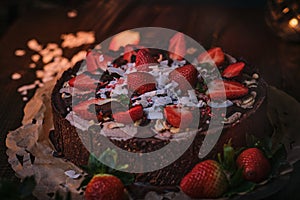 Vegan and tasty chocolate cake with strawberries, cocnut shovel and raspberry seeds, served on a paper serviette