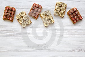 Vegan toasts with peanut butter, fruits and chia seeds over white wooden background, top view. Healthy breakfast, dieting concept.