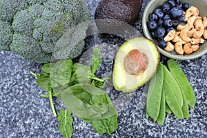 Vegan vegetarian plant based diet selection of cashew nuts, blueberries, spinach, mange tois peas avocado and broccoli on marble a