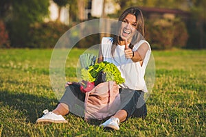 Vegan woman sitting on the grass with pink reusable bag with fresh vegetables