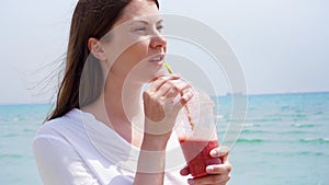 Vegan woman with strawberry smoothie against sea in slow motion. Fit female enjoy healthy lifestyle