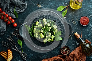 Vegans salad with cucumber and dill on a black plate. Rustic style. Top view.