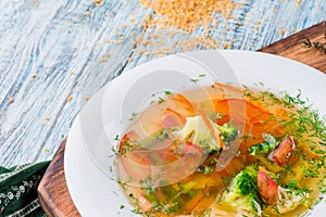 Vegetable broth, soup with broccoli, asparagus, carrots, onions, bell peppers and greens in white plate