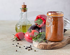 Vegetable caviar in jar, fresh eggplants, bell pepper, tomatoes and thyme on wooden board. Homemade preserves. Vegetarian cuisine