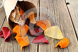 Vegetable chips spilling from a paper cone on rustic wood