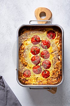 Vegetable clafoutis in baking dish on concrete background, savory pie with cabbage and whole cherry tomatoes .  Vegetarian cuisine