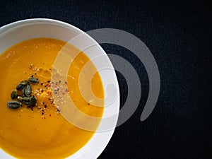 Vegetable cream made with pumpkin and carrot, decortated with pepper and pumpkin seeds on a dark background