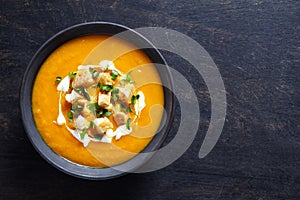 Vegetable cream pumpkin soup with carrot and crackers. Top view on a dark creative background. Healthy diet meal.