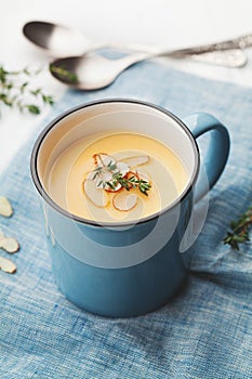 Vegetable cream soup from carrot and potato decorated almonds flakes in blue bowl on rustic background.