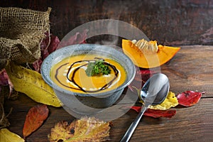 Vegetable cream soup from red kuri squash with parsley garnish in a blue bowl on dark rustic wood with autumn leaves, copy space,